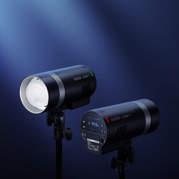 Two black studio lights on stands illuminated against a dark blue background with a spotlight effect.