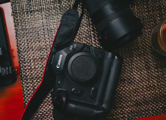 Canon EOS R1 camera with lens and cup of coffee on a woven mat.