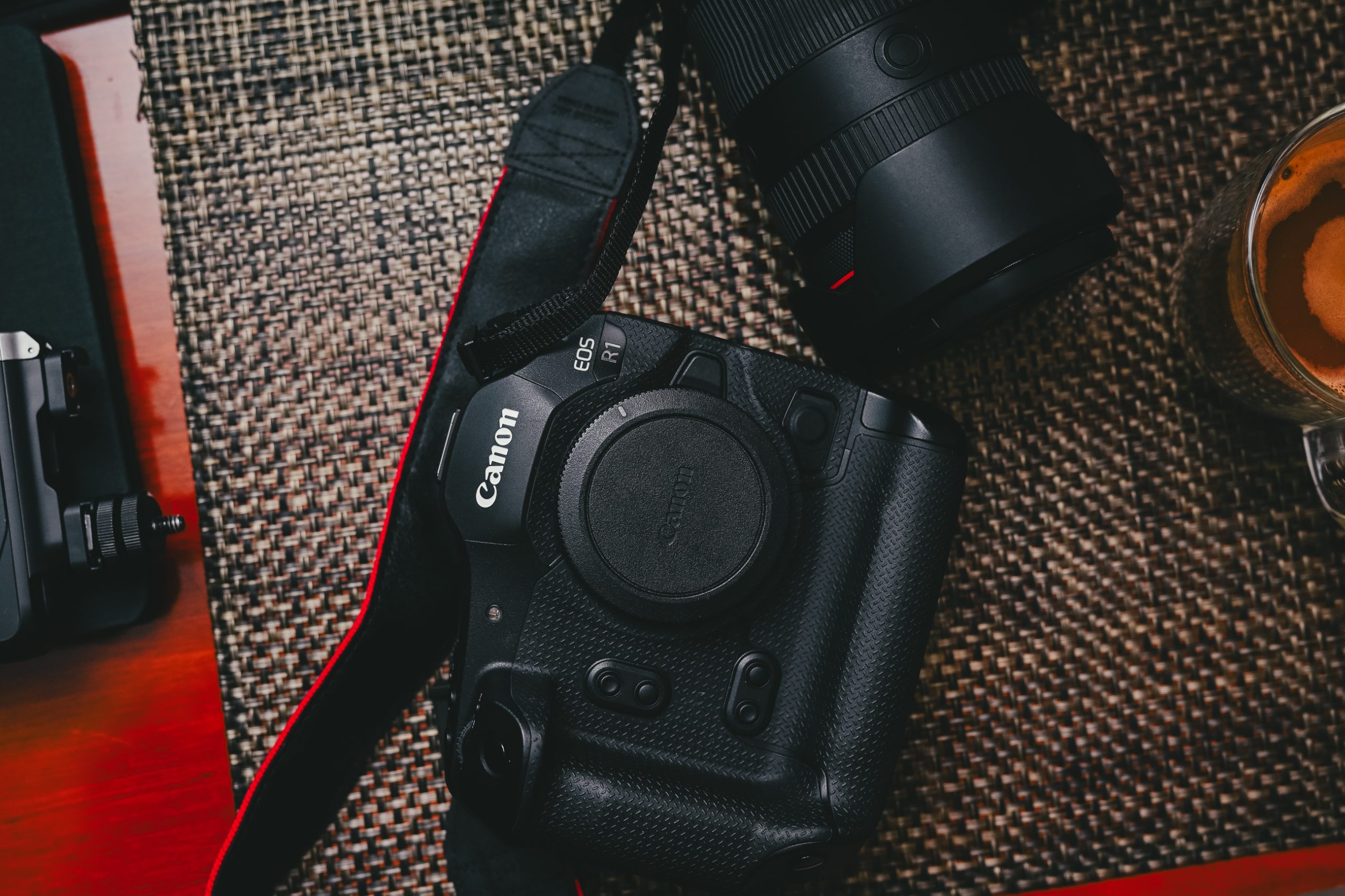 Canon EOS R1 camera with lens and cup of coffee on a woven mat.