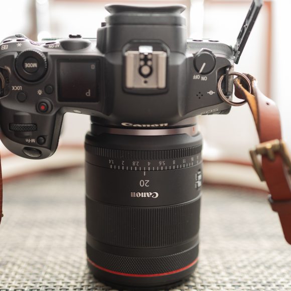 Top view of a Canon camera with a 20mm lens and brown leather strap on a textured surface.