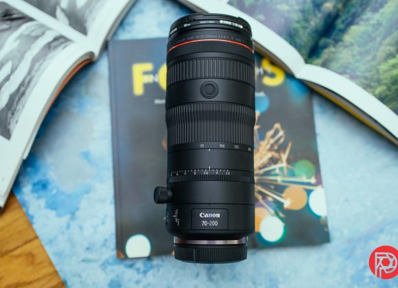Canon 70-200mm camera lens placed on a magazine, with open books in the background.