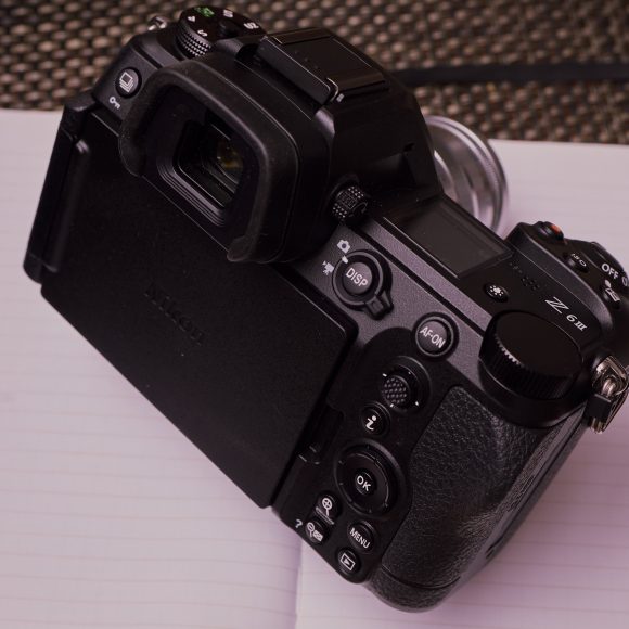 A black digital camera rests on an open blank notebook with a textured background and a red circular logo.