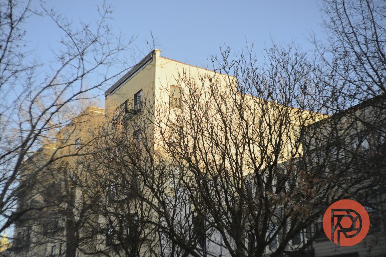Yellow building behind leafless trees under a clear blue sky, with sunlight casting shadows on the facade.