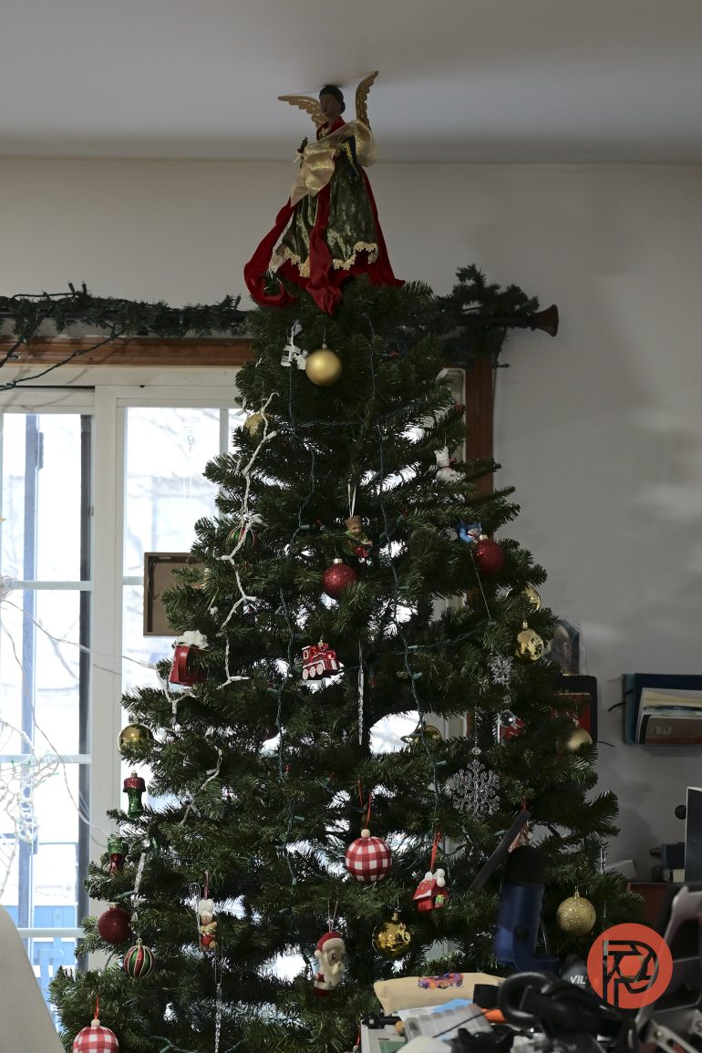 A decorated Christmas tree with an angel topper stands by a window in a cozy room.