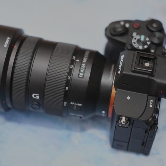 Sony Alpha camera with a large lens resting on a light blue surface, viewed from above.