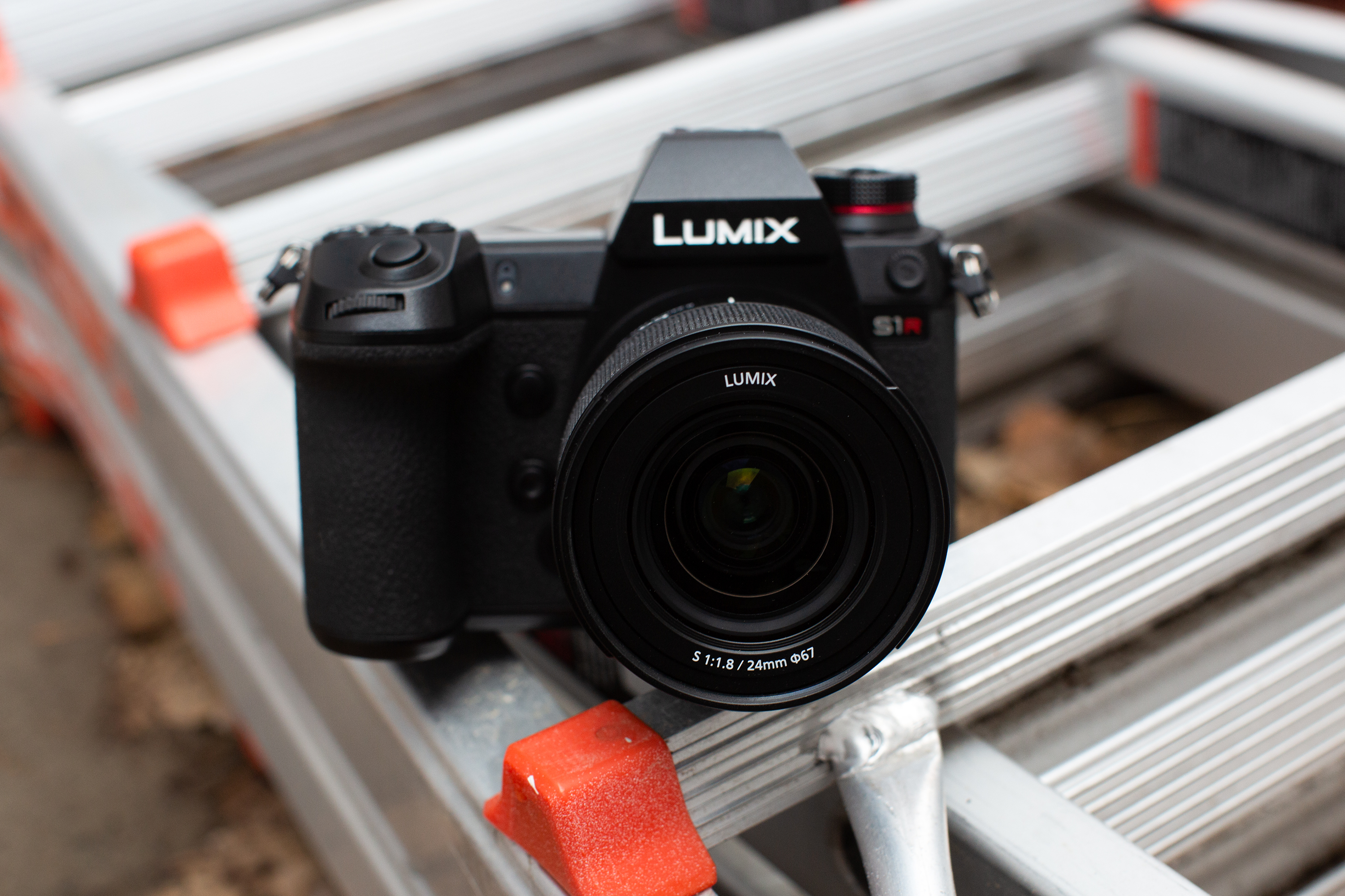 A Lumix S1R camera sits on a metal ladder with orange safety caps.