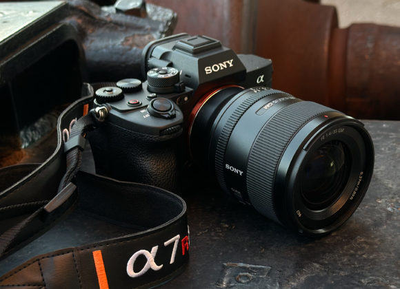A Sony Alpha camera with a zoom lens and branded strap resting on a metal surface.