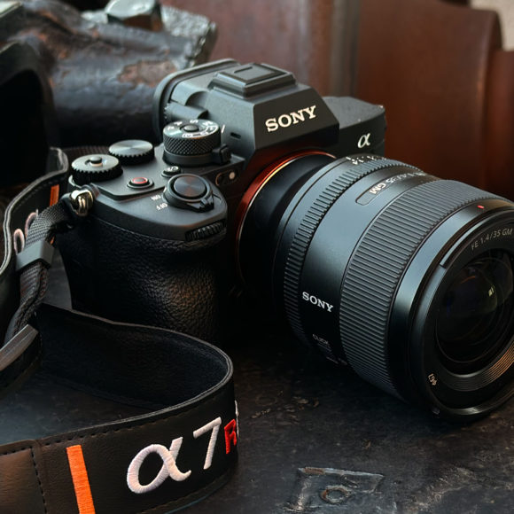 A Sony Alpha camera with a zoom lens and branded strap resting on a metal surface.