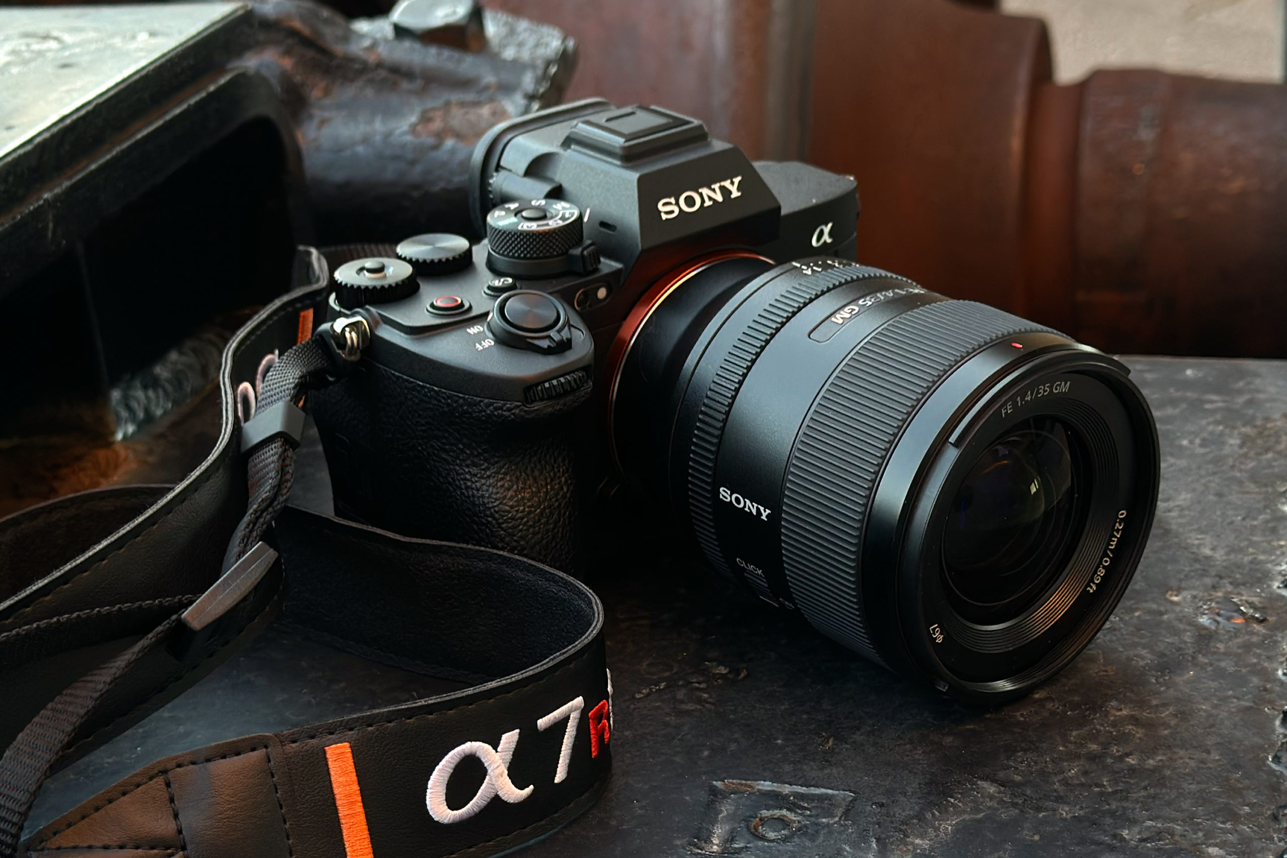 A Sony Alpha camera with a zoom lens and branded strap resting on a metal surface.