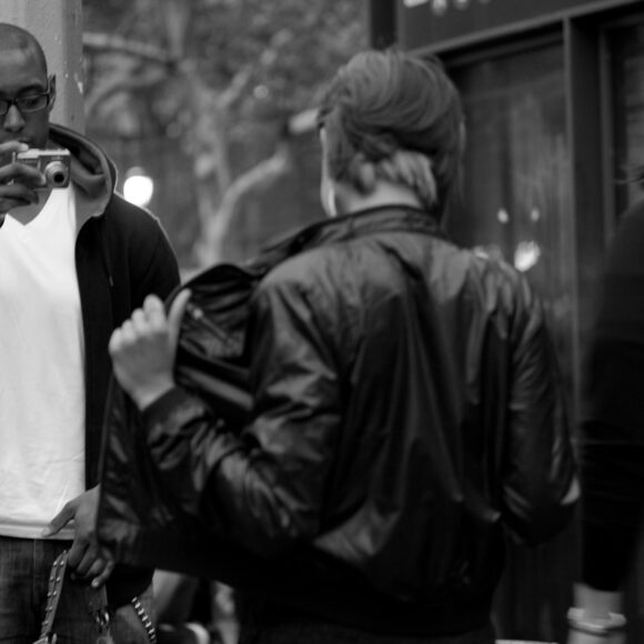 Man taking a photo on a street as a person adjusts their jacket.