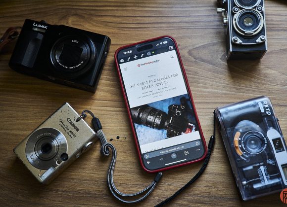 A smartphone and four cameras are arranged on a wooden surface.