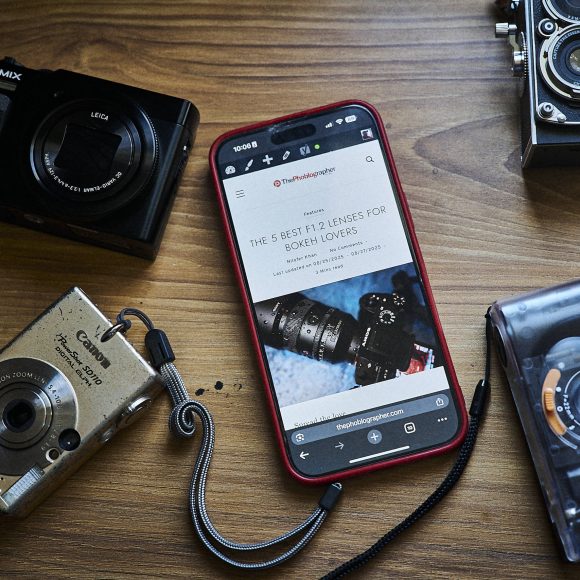 A smartphone and four cameras are arranged on a wooden surface.