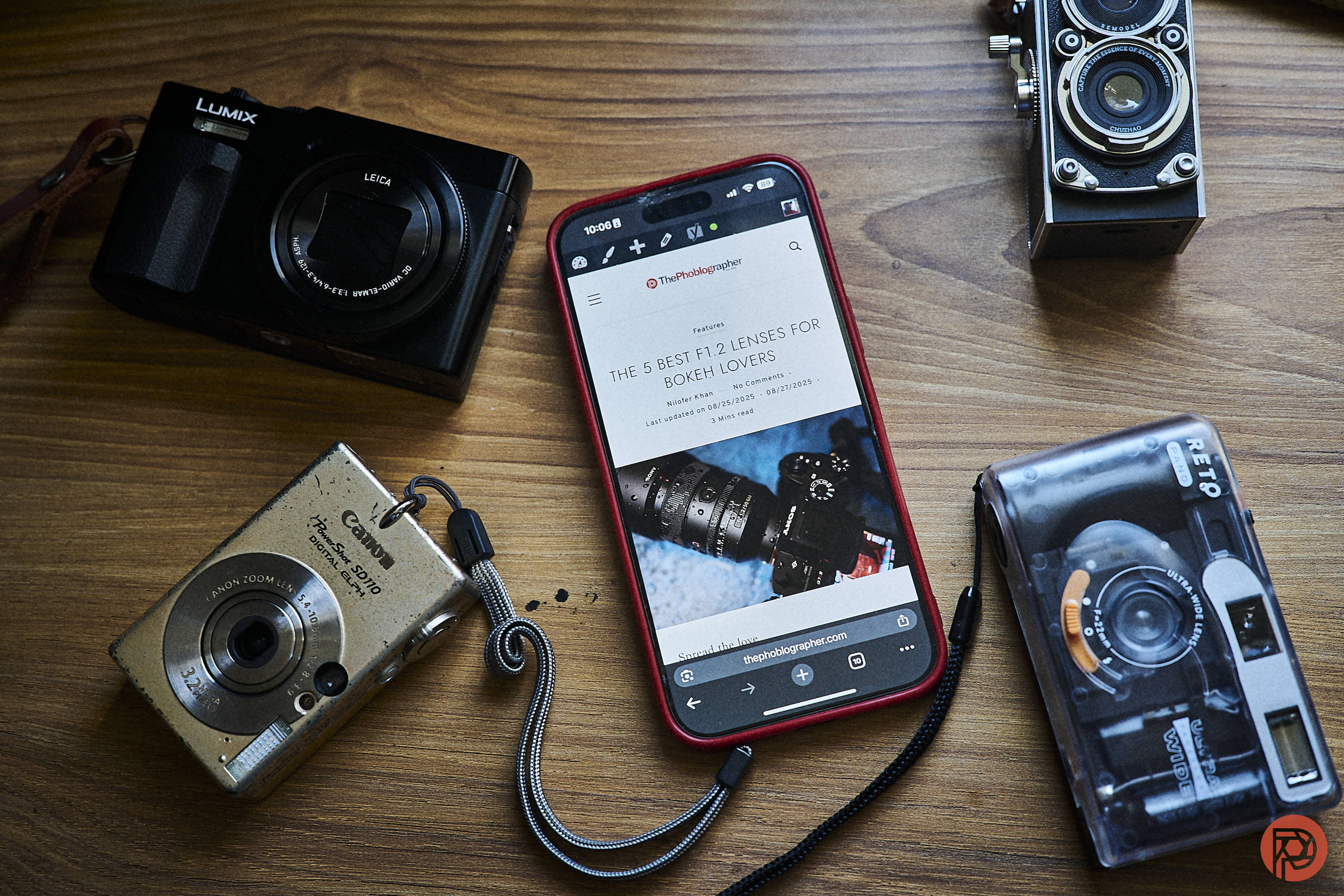 A smartphone and four cameras are arranged on a wooden surface.