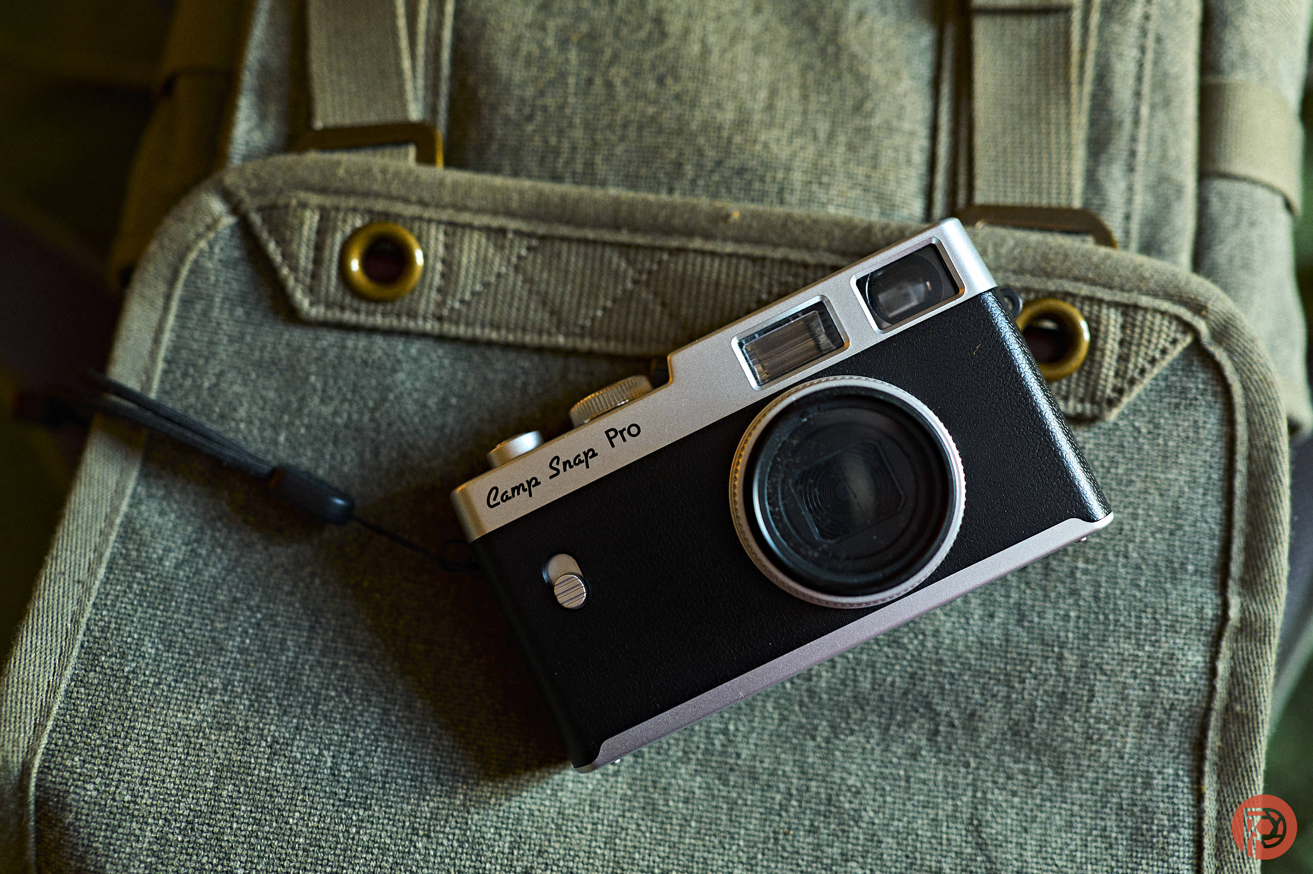 A vintage black camera labeled Camp Snap Pro rests on a green canvas backpack.