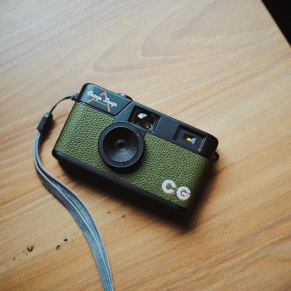 A green vintage film camera with a wrist strap rests on a wooden surface.