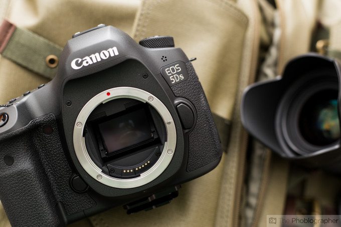 Close-up of a Canon EOS 5DS camera body without a lens, next to a detached camera lens.