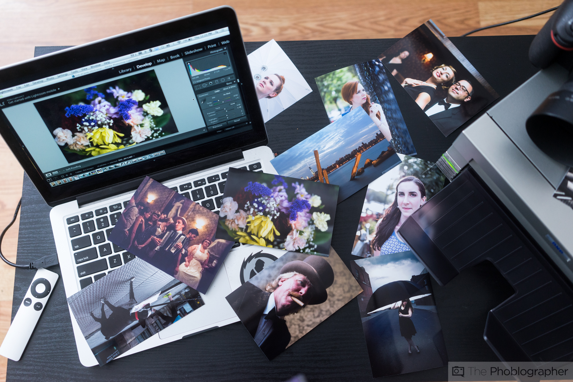 Laptop with photo editing software open, surrounded by printed photos on a table.