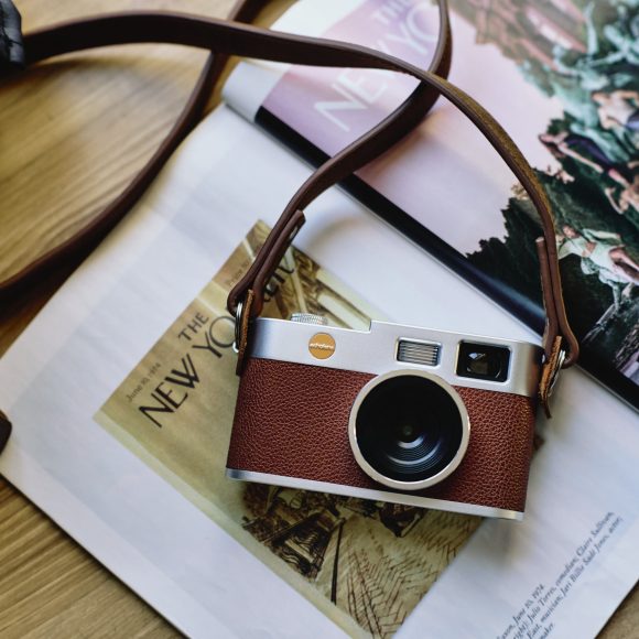 A vintage-style camera with a brown strap rests on an open magazine on a wooden surface.