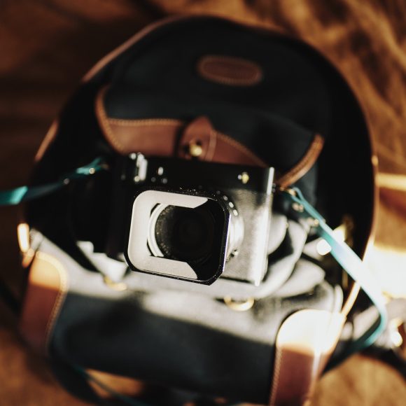 A camera resting on a backpack with sunlight casting shadows across both items.