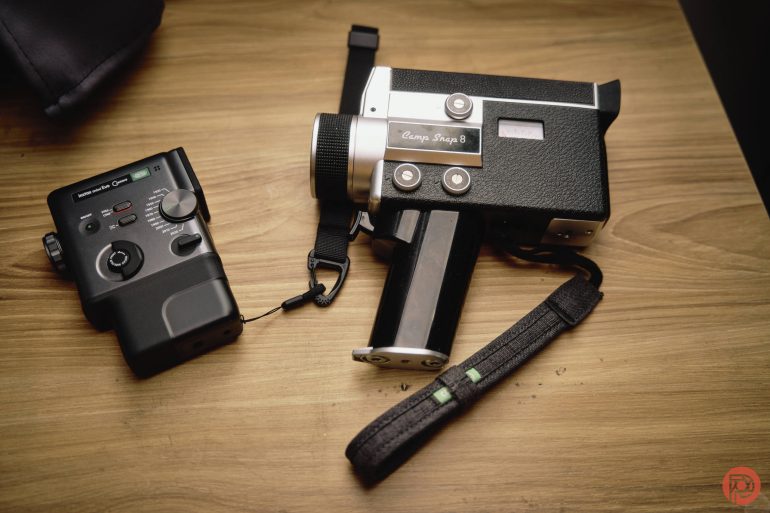 A vintage black film camera and a black audio recorder rest on a wooden surface.