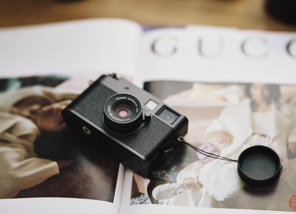 A black camera with a lens cap sits on an open fashion magazine featuring images of models in stylish outfits.