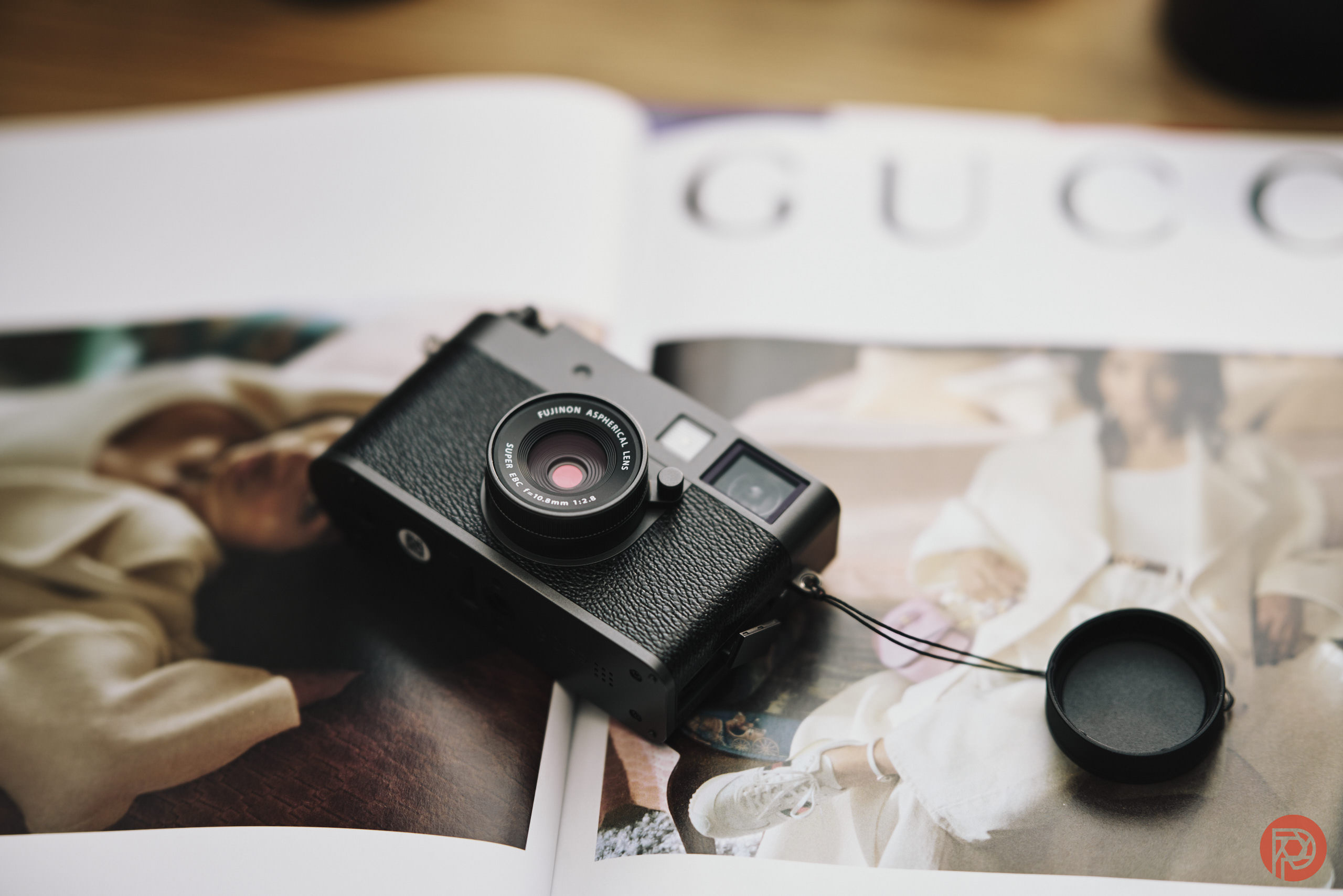 A black camera with a lens cap sits on an open fashion magazine featuring images of models in stylish outfits.