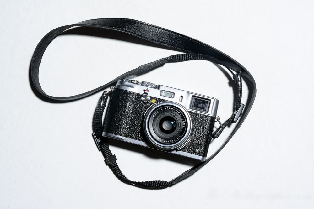 Vintage-style camera with a black body, silver details, and a black strap, on a plain white background.