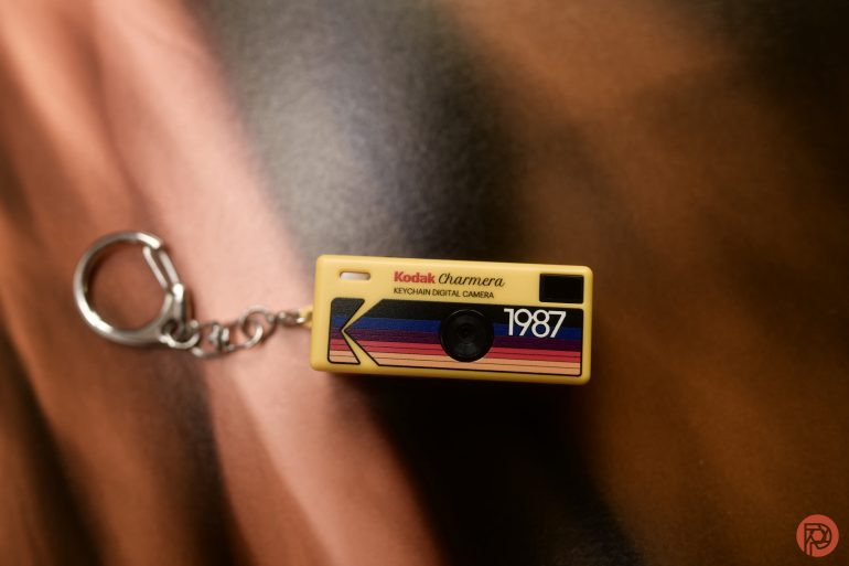A Kodak Chamera 1987 keychain shaped like a vintage camera on a brown surface.