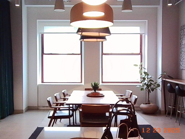 A modern dining room with a wooden table, chairs, pendant lights, and large windows letting in natural light.