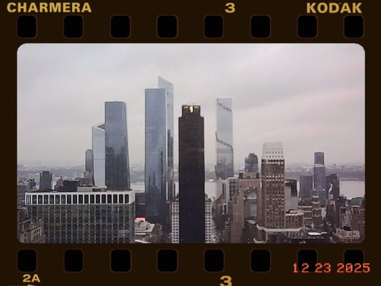 City skyline with modern skyscrapers on a cloudy day, viewed through a film camera frame.
