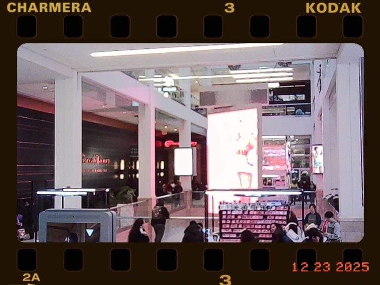 A busy shopping mall with bright digital billboards and people walking or browsing stores.