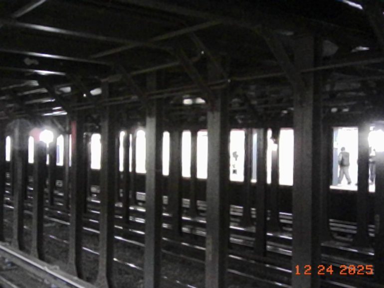 Subway tracks and beams with people waiting on a platform in the background, photo dated 12-24-2025.