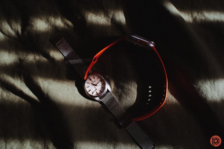 A wristwatch and a smartwatch placed together on a dark, striped fabric with light and shadow.