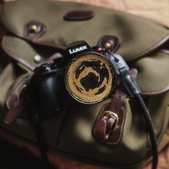 A camera with a lens cap sits on a tan bag with brown straps, seen from above.