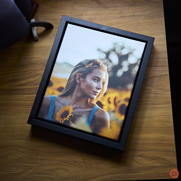 Framed photo of a woman holding a sunflower, resting on a wooden table.