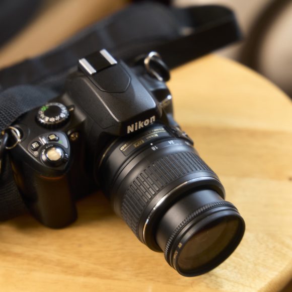 A Nikon DSLR camera with a zoom lens and strap rests on a round wooden table.