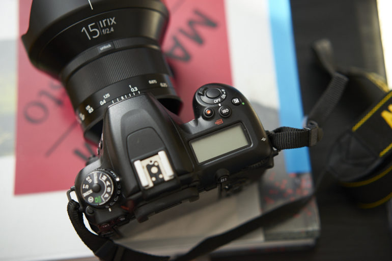 A DSLR camera with a lens attached rests on top of stacked books and a camera strap.