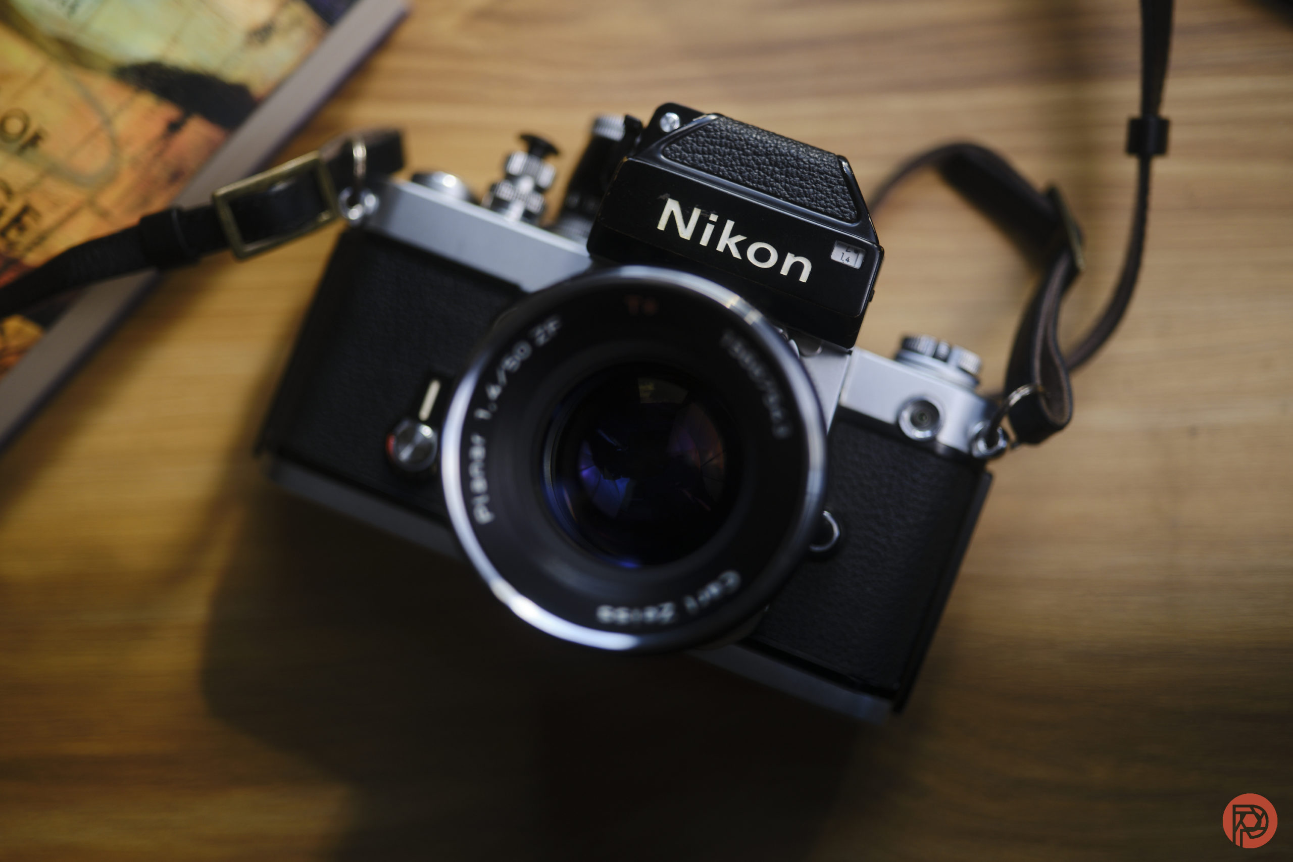 Vintage Nikon film camera with a lens and strap, placed on a wooden surface near a book or map.