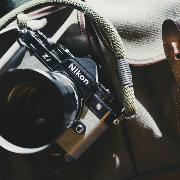 A Nikon ZF camera with a green strap rests on a brown bag with leather buckle details.