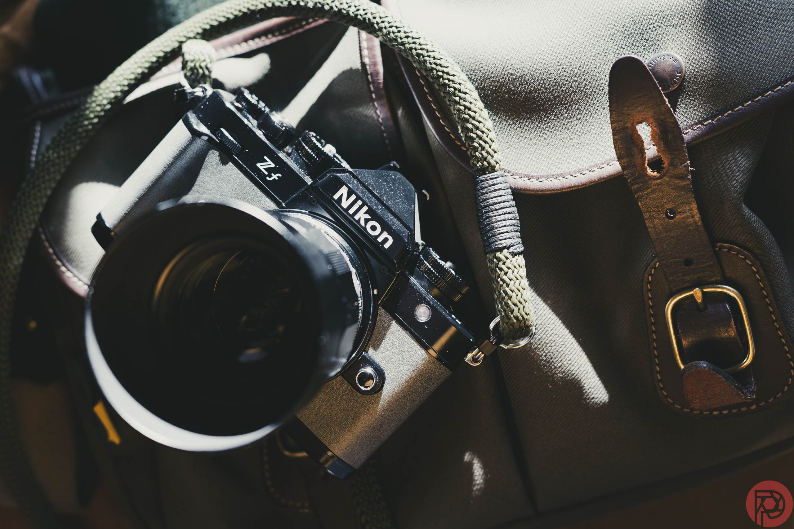 A Nikon ZF camera with a green strap rests on a brown bag with leather buckle details.