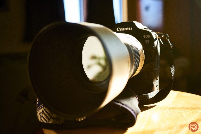 Canon EOS R3 camera with a large lens rests on a wooden surface in warm light.