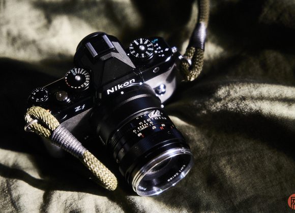 A Nikon Zf camera with a lens and strap lies on a textured green fabric.