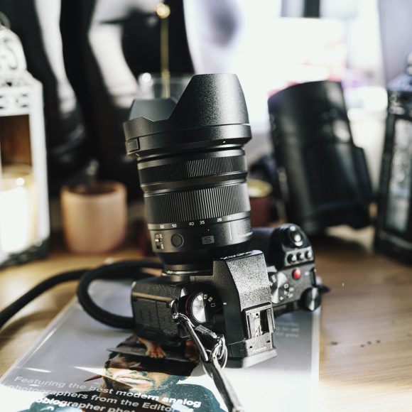 A black camera with a large lens sits on a wooden table surrounded by candles and lanterns.