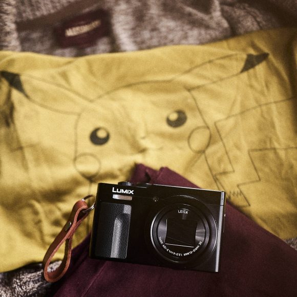 A Lumix camera rests on a yellow Pikachu shirt and a maroon jacket with a gray sweater in the background.