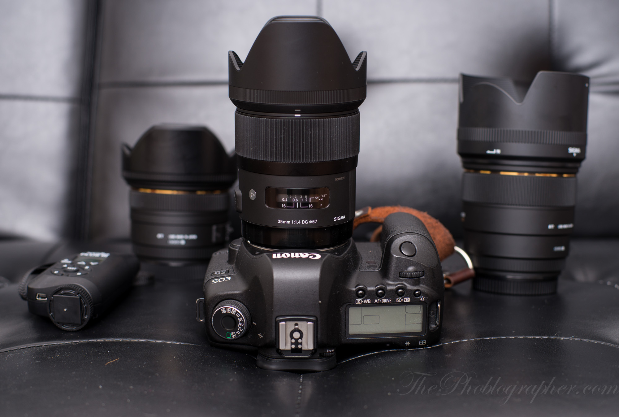 A Canon camera with three lenses and a remote control, arranged on a black leather surface.