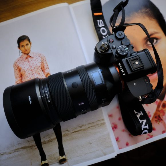 A camera with a large lens sits on an open magazine displaying photos of a woman in a floral shirt.