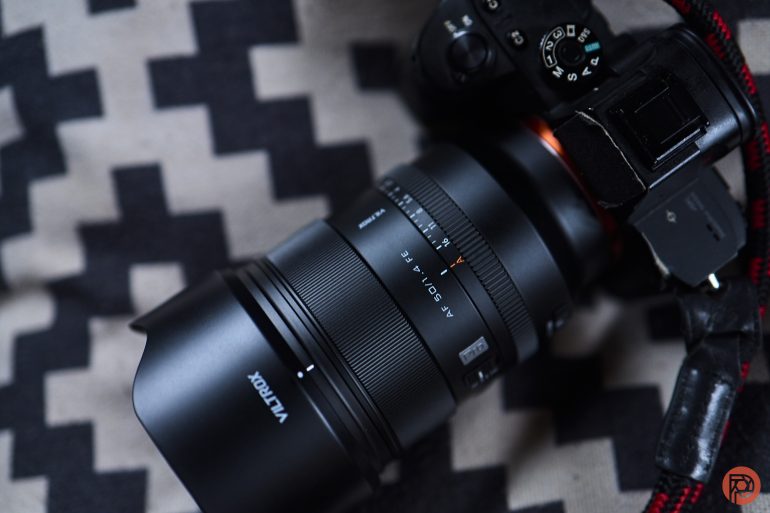 A Viltrox camera lens attached to a black camera rests on a zigzag-patterned fabric background.