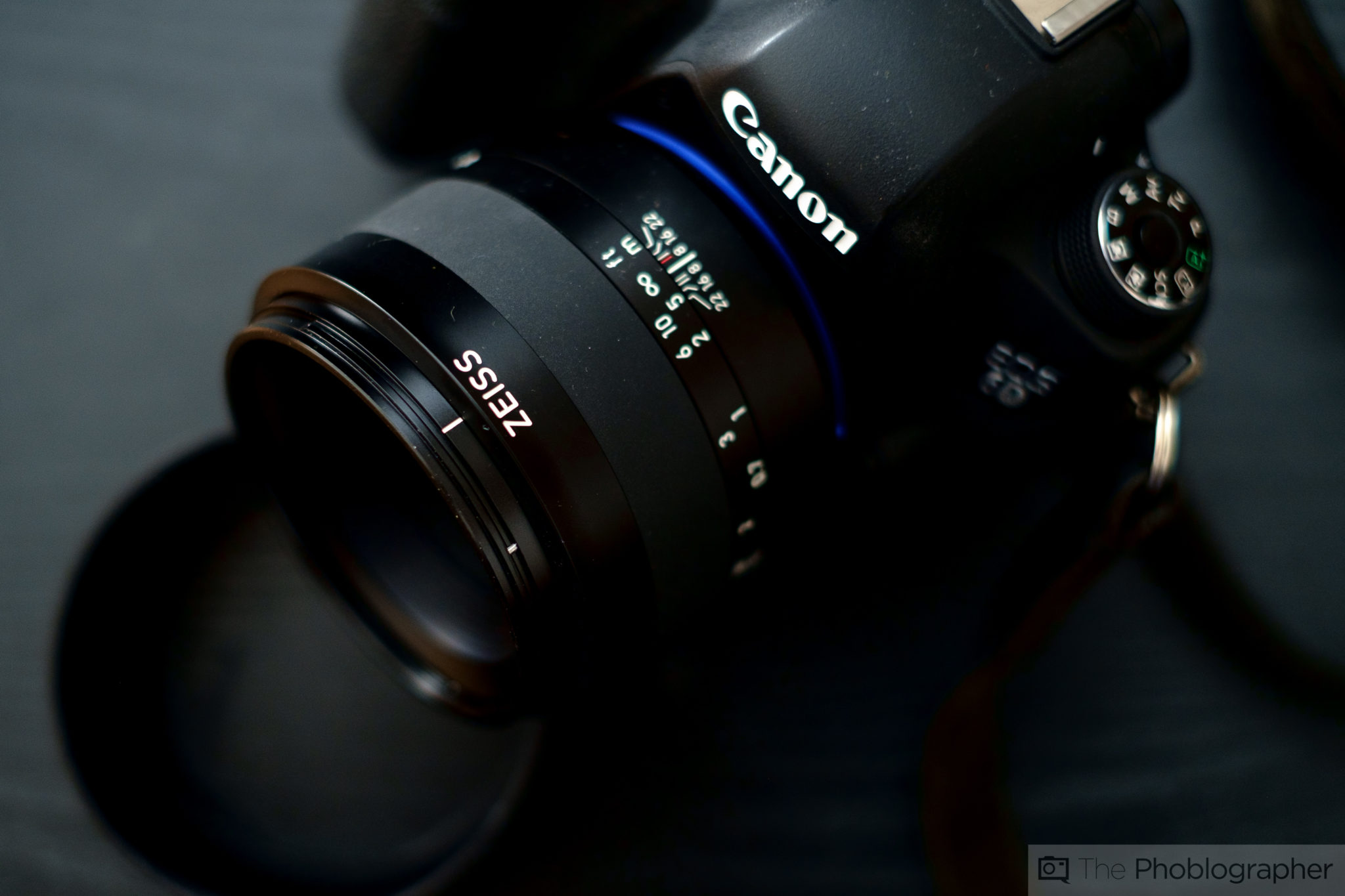 Close-up of a Canon DSLR camera with a Zeiss lens on a dark surface.