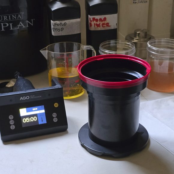 A film developing setup with chemicals, timer, and a developing tank on a white surface.