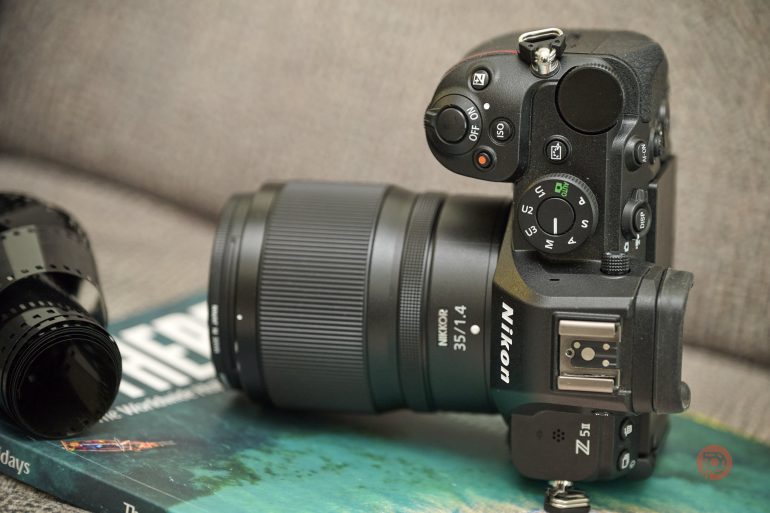 A Nikon Z5 II camera with a 35mm lens rests on a magazine beside a detached camera lens.